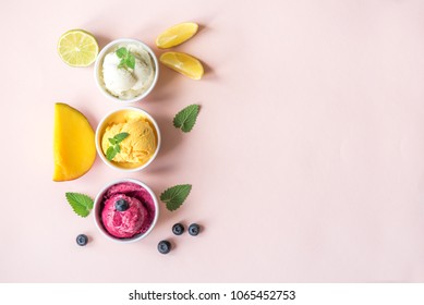 Three Various Fruit And Berries Ice Creams On Pink Background, Copy Space. Frozen Yogurt Or Ice Cream With Lemon, Mango, Blueberries - Healthy Summer Dessert.