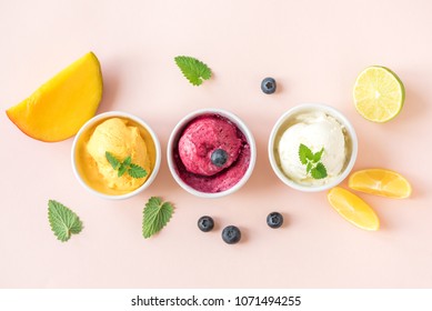 Three various fruit and berries ice creams on pink background, copy space. Frozen yogurt or ice cream with lemon, mango, blueberries - healthy summer dessert.