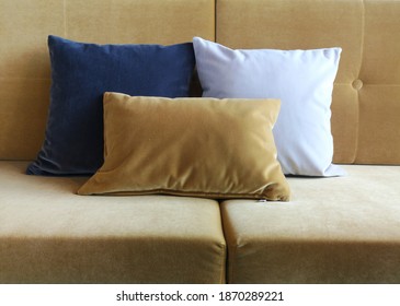 Three Velvet Cushions On A Velvet Sofa In The Colors Blue, Yellow And White. 