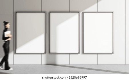 Three vertical blank posters on a grey tiled wall, a woman walking by holding a notepad. Modern design, concept of advertising, empty template