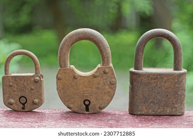 three very old rusty reliable different retro padlocks on a wooden surface on a green background outdoors in the summer afternoon
