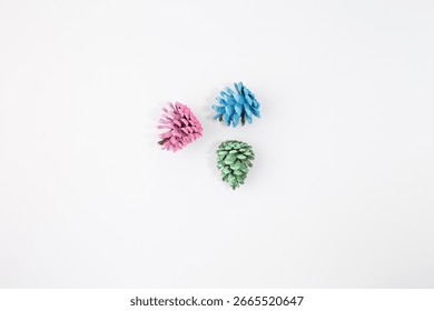 three vibrantly painted pine cones set against a white background. Each pine cone is a different color pink, blue, and green, DIY blogs, and creative product 