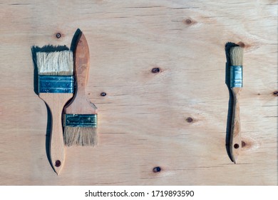 Three Vintage Brushes With Bristles Against Wooden Plywood Background. Tools For DIY Painting Project