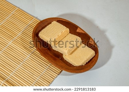 three wafers of vanilla flavor arranged in a row on a wooden plate with a bamboo roll in the background