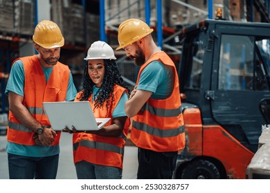 Three warehouse workers are analyzing data on a laptop, working together to improve efficiency and productivity in a busy industrial setting - Powered by Shutterstock