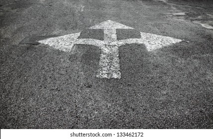 A three way arrow symbol on a black asphalt road surface.