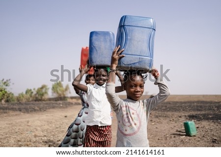 Three West African Pretty Girls,returning to the village, carrying plastic water containers on their heads.Water Supply in Rural Communities.