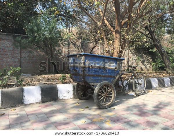 A three wheels loading cycle left beside road\
divider near trees