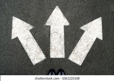 Three white arrows pointing in different directions on gray asphalt floor and black Shoes. Making decisions and making choices. Find your own way. Walking direction, crossroads, intersection, crossway