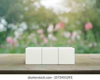 Three white block cubes on wooden table over blur pink flower and tree in garden