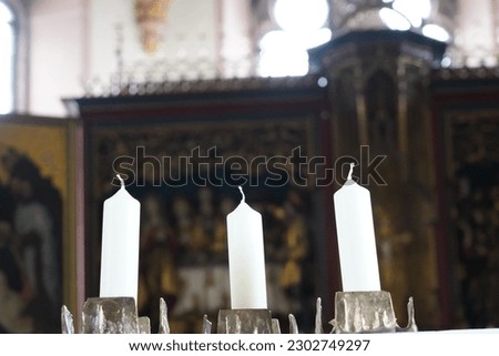 Three white candles placed in a chandelier in a church. On the background there is defocused altar.