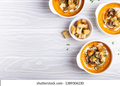 Three White Ceramic Bowls With Pumpkin Cream Soup Puree With Mushrooms, Croutons And Heavy Cream On White Wooden Rustic Background, Top View, Close-up. Family Dinner And Comfort Food, Space For Text