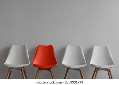 Three White Chairs And Red On Gray Wall Background In Office Or Room. Row Of Stools With One Of Different Colour. Job Opportunity, Recruitment, Business, Leadership And Hiring Concept, Copy Space