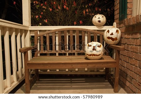 Three white jack o'lanterns on a wooden bench waiting for halloween