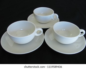 Three White Mid Century Modern Ceramic Coffee Cups And Saucers On A Black Limbo Background 