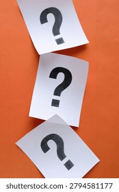 Three white paper notes with question marks arranged vertically on orange background