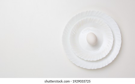 Three white plates of different sizes on top of each other. On the last one is a white egg. Concept - healthy, easter. Copy space