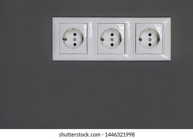 Three white Power sockets with frame on dark grey wall as a background. Minimalism concept