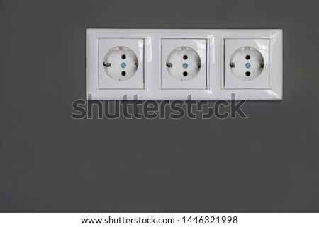 Three white Power sockets with frame on dark grey wall as a background. Minimalism concept