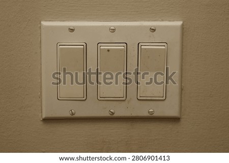 Three white toggle light switches on a beige textured wall. A common household utility