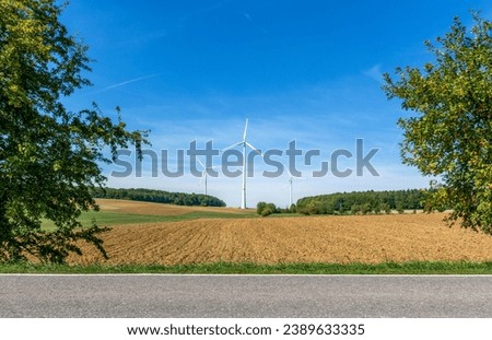 Three wind energy turbines standing in a reordered field with a country road in foreground in spring in Saarland Germany