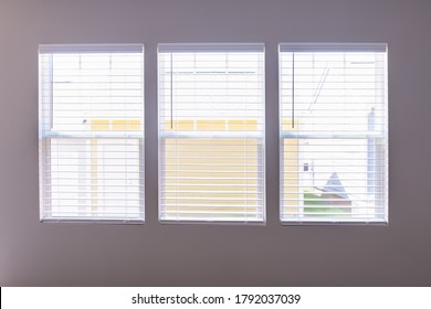 Three Windows With Closed Modern White Wood Faux Window Blinds As Background.