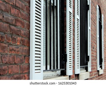 Three windows on a red brick wall of an old building with open white wooden shutters in the street.