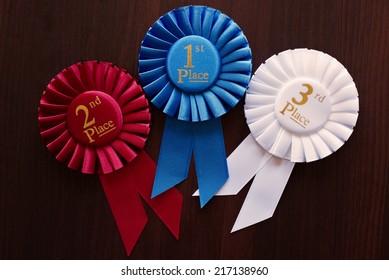 Three winners rosettes for first, second and third place in pleated blue, red and white ribbon respectively with central text
