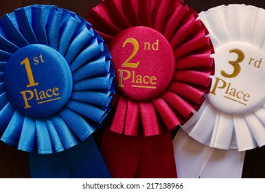 Three winners rosettes for first, second and third place in pleated blue, red and white ribbon respectively with central text