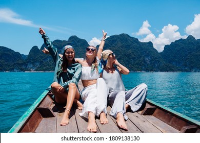 Three Woman Tourists Friends Travel Around Khao Sok National Park, On Vacation In Thailand. Sailing On Asian Boat On Lake At Sunny Day, With Amazing View. 