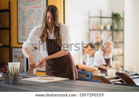 Three women in aprons working at pottery, kneading clay and making earthenware at workshop