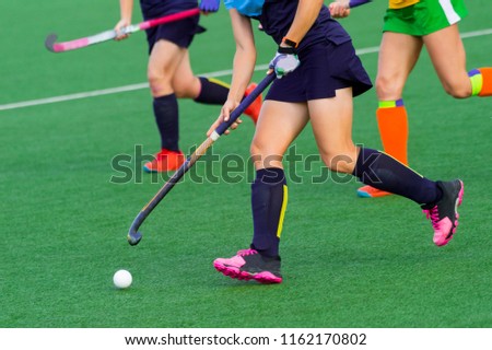 three women battle for control of ball during field hockey game