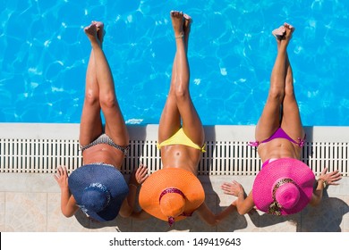 Three women in bikini wearing a straw hat by the swimming pool