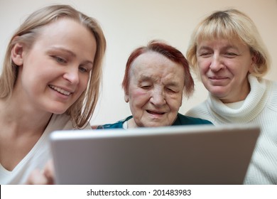 Three Women Of Different Ages Smiling Using A Smart Tablet