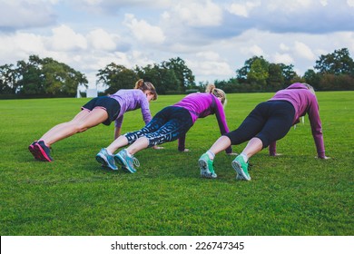 Three women are doing push ups on the grass in the park - Powered by Shutterstock