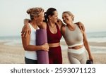 Three women dressed in activewear and sharing a joyful moment together on the beach after practicing yoga, exemplifying friendship and vitality outdoors.