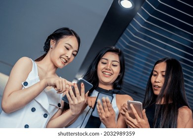 Three Women Friends Having Conversation While Looking At Mobile Phone In Their Hands. Concept Of Social Media, Gossip News And Online Shopping.