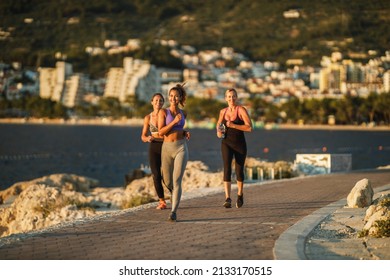 Three Women Friends Are Jogging Along The Sea Shore And Enjoying In Summer Sunny Day.