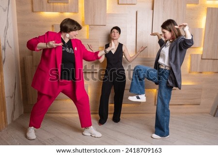 Three women participate in a corporate business game, pretending to be a battle. Group of three individuals appears to be dance battle, featuring dynamic poses.