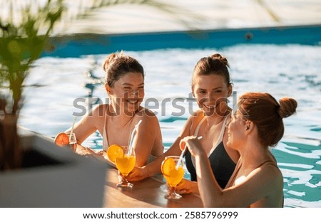 Three women relax in a pool, laughing and sipping colorful cocktails while enjoying the warm weather. The vibrant atmosphere enhances their cheerful spirits