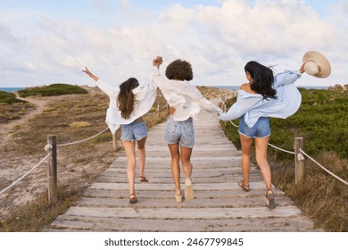 Three women are running on a wooden boardwalk, with one of them wearing a hat. Scene is joyful and carefree, as the women are enjoying their time together outdoors - Powered by Shutterstock