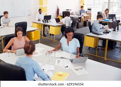 Three women share a desk in a busy office, elevated view