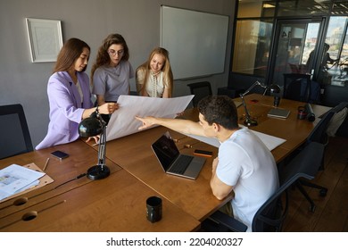 Three Women Studying Large Sheet Of Paper Next To Man