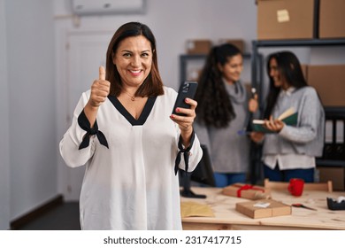 Three women working at small business ecommerce smiling happy and positive, thumb up doing excellent and approval sign  - Powered by Shutterstock