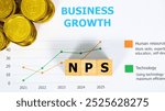 Three wooden blocks with the word NPS on a graph sheet with a pile of gold coins, abbreviation for Net Promoter Score. Growth business and investment. Business and financial market concept.