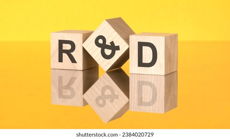 three wooden cubes with acronym R and D on yellow background. reflection of an image on a glass surface concept