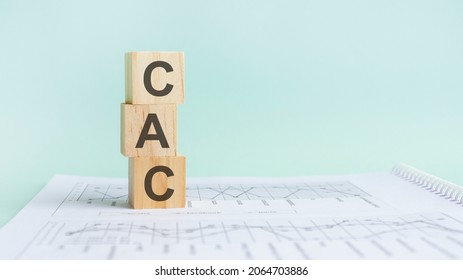 three wooden cubes with letters CAC, on white table and diagram, business concept. CAC - short for customer acquisition cost