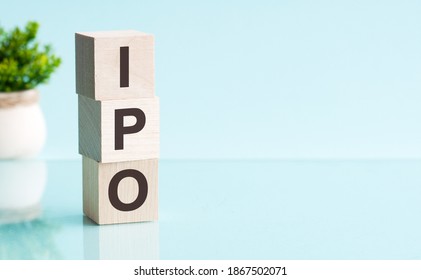 Three wooden cubes with letters - IPO - short for initial public offering, on blue table, space for text in right. Front view concepts, flower in the background.