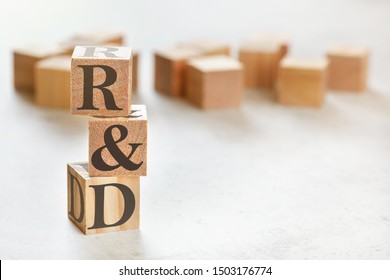 Three wooden cubes with letters R&D (means Research & Development ), on white table, more in background, space for text in right down corner