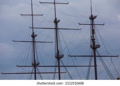 three wooden masts of a Dutch fluyt merchant sailing ship of XVIII century on a grey sky and clouds background close up view